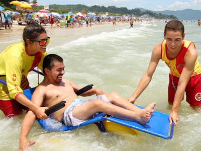 Foto: Bombeiros auxiliando cadeirante na praia.